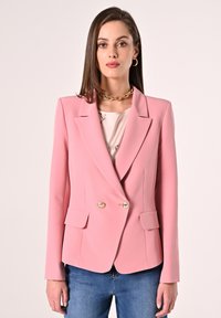 Rosa maßgeschneiderte Blazer mit strukturierten Schultern, goldenen Doppelknebeln und zwei Fronttaschen, kombiniert mit einem hellen Oberteil und blauen Jeans.