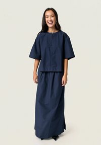 Navy two-piece outfit featuring a cropped top with wide sleeves and a long skirt, constructed from textured fabric with a side slit.