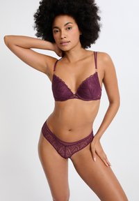 Ensemble de lingerie bordeaux comprenant un soutien-gorge en dentelle avec un bord festonné et un motif floral complexe, assorti à une culotte semi-transparente.