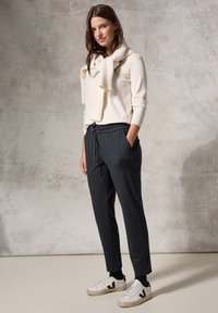 Beige sweater with a knit texture over a white shirt, paired with dark pinstriped trousers and white sneakers with black accents.