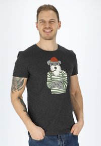 T-shirt grigia a maniche corte con un cane dei cartoni animati che indossa un cappellino rosso e un maglione a righe, con illustrazioni dettagliate sul maglione.