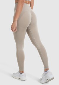Beige hoch taillierte Leggings mit einem strukturierten Muster an den Unterschenkeln. Tragen Sie sie mit weißen Sportschuhen und zeigen Sie ein figurnahes Design.