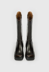 Καφέ δερμάτινα μποτάκια μέχρι το γόνατο με λεία υφή, τετράγωνη μύτη, διακοσμητικό φερμουάρ στο πλάι και χοντρή μαύρη ελαστική σόλα.