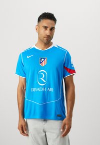 Blue athletic jersey with white accents, featuring a round neck, club logo, sponsor text, and short sleeves. Made of lightweight fabric.