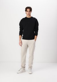 Zwarte crewneck sweatshirt, beige cargo pants met zijzakken en witte sneakers. De outfit heeft een ontspannen pasvorm en een eenvoudig ontwerp.