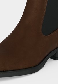 Bottine en daim marron avec panneau latéral élastique noir et petit talon bloc noir.