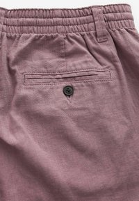 Lilla linnedrenge med elastisk talje, der har en baglomme med en enkelt sort knap. Glat, tekstureret stof.