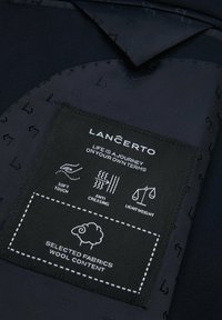 Granatowy materiał o gładkiej teksturze z czarną etykietą z białym tekstem i ikonami oznaczającymi 'miękki dotyk', 'odporny na zagniecenia' oraz 'lekki'.