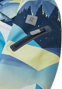 Rękaw niebieskiej i żółtej kurtki z wzorami gór i gwiazd, z zamkniętą kieszenią i odblaskowym kwadratowym logo.