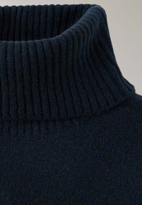 Gros plan sur le col roulé côtelé bleu marine foncé avec une texture épaisse et verticale en maille.