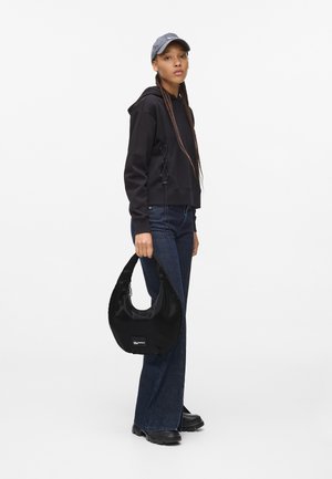 Felpa nera corta con dettagli laterali, abbinata a jeans svasati blu scuro. Borsa hobo nera lucida con logo e scarpe nere.