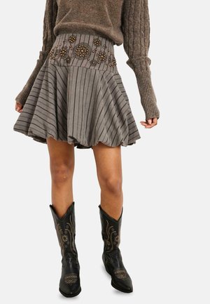 Falda acampanada hasta la rodilla con rayas verticales y detalles florales con cuentas, combinada con suéter marrón de punto trenzado y botas negras bordadas.