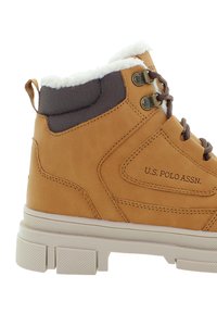 Hnědozlatá syntetická kožená bota s bílým fleecovým límcem, šedou polstrovanou částí, hnědými tkaničkami, kovovými očičkami a texturovanou bílou podrážkou.