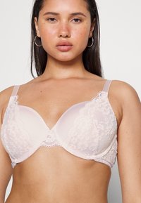 Lace-trimmed, padded bra in soft pink with sheer cups and adjustable straps. Features floral patterns and scalloped edges.