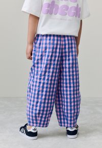 Geruite broek in blauw en roze katoen met een losse pasvorm. Draagt met zwarte sneakers met witte accenten.