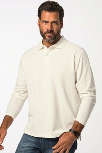 Langærmet polo-shirt i cremefarve, lavet af blødt stof, med krave og placket med tre knapper. Båret sammen med mørke jeans.