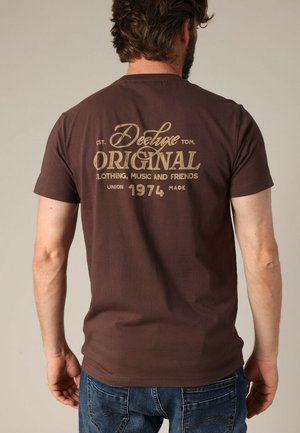 Bruine katoenen t-shirt met een groot gouden logo op de achterkant, met korte mouwen en een klassieke pasvorm.