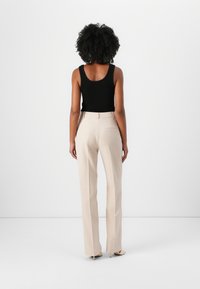 Black sleeveless top paired with high-waisted, straight-leg beige trousers. The outfit features a smooth texture and minimalistic design.