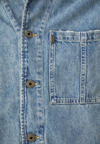 Gaiši zils denima krekls ar priekšējo kabatu, bronzas pogām un vieglu nolietojumu. Uz kabatas ir zīmola "Pepe Jeans" logo.