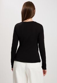 Czarna długa bluzka z długim rękawem i okrągłym dekoltem, dopasowana, w połączeniu z białymi spodniami o wysokim stanie z naszytymi tylnymi kieszeniami.