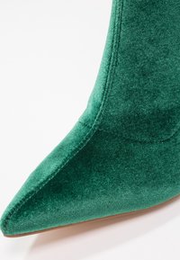 Bottine en velours vert avec un bout pointu et une texture lisse. Présente un design sans coutures et un détail subtil de couture le long des bords.