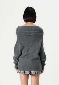 Suéter gris de gran tamaño con un amplio escote caído y puños acanalados, combinado con una falda de mezclilla de volantes en capas. Tejido de punto con textura.