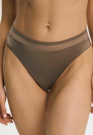 Środkowa część ciała kobiety w wysokich, brązowych majtkach z szerokim pasem i gładkim materiałem na jednolitym tle.