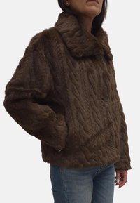 Giacca in finta pelliccia marrone con un motivo a maglia a treccia testurizzato, colletto oversize e due bottoni, abbinata a jeans di denim.