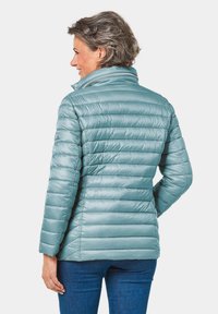 Giacca trapuntata azzurro chiaro con un design a imbottitura, colletto alto e una morbida lucentezza. Presenta maniche lunghe e una silhouette aderente.