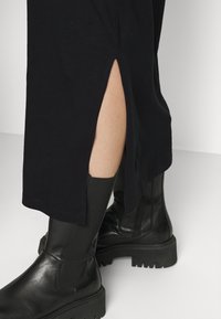 Czarna, długa do kostek sukienka z detalem w postaci rozporku z boku, zestawiona z teksturowanymi czarnymi skórzanymi botkami na grubej podeszwie i z zamkiem błyskawicznym.