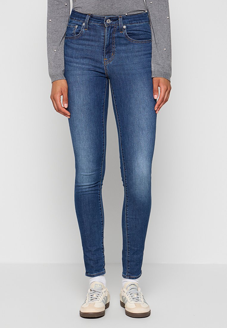 Hautenge Jeans aus mittelblauem Denim, mit klassischem Fünf-Taschen-Design und tailliertem Schnitt. Kombiniert mit beigefarbenen Sneakers.
