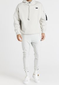 Felpa grigia chiara con cappuccio regolabile e tasca frontale. Abbinata a pantaloni felpati slim-fit dello stesso colore. Sneakers bianche completano il look.