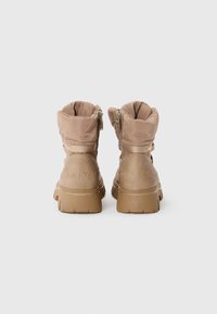 Beige insulated ankle boots with a padded collar, dual zippers, textured faux leather, and a chunky rubber sole. Logo embossed on the heel.