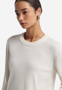 Weißer Rundhalsausschnitt-Pullover aus weichem Strickstoff. Mit geripptem Ausschnitt und langen Ärmeln, samt einer glatten Oberfläche und minimaler Dekoration.