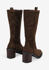 Stivali al ginocchio marroni in suede con tacco impilato in legno scuro e zip laterale, caratterizzati da una texture liscia e minimi dettagli di cucitura.