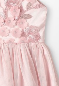 Růžové šaty s přiléhavým živůtkem, zdobené vyšívanými květinovými motivy a flitry. Plynná tylová sukně vytváří vrstvenou texturu.