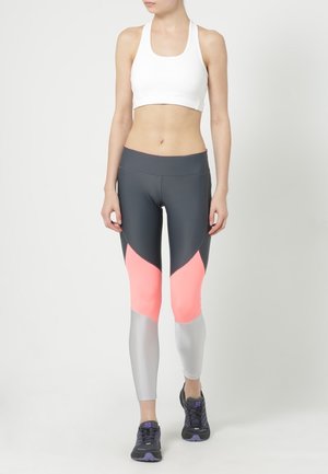 Szare i koralowe legginsy sportowe z designem w kolorach bloku oraz białym stanikiem sportowym. Legginsy mają srebrny fragment i elastyczny krój.