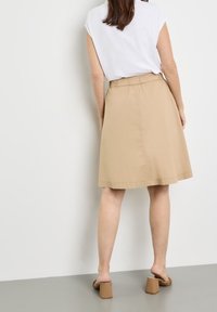 Beige hame mittaiseen, jossa on elastinen vyötärö, valmistettu sileästä materiaalista. Yhdistettynä valkoiseen toppiin ja ruskeisiin lohko-nuorisokenkiin.