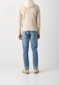 Light beige ribbed hoodie with a hood, paired with light blue denim jeans. Footwear is tan and gray sneakers. Minimalistic design.