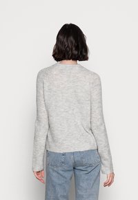 Grijze gebreide trui met lange mouwen, ronde halslijn en een iets verkorte zoom. Gestructureerde afwerking en zachte stof. Draagt met blauwe jeans.