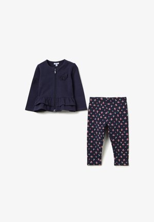 Marine blauwe zip-up jas met peplumrand en bloemaccent, gecombineerd met marineblauwe leggings met een klein roze en witte bloemenpatroon.