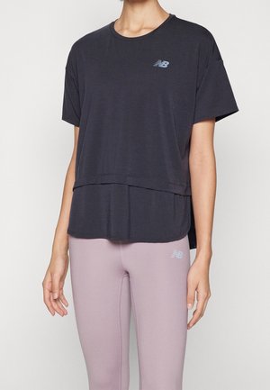 Persona que lleva una camiseta negra holgada de manga corta de New Balance y leggings de color púrpura claro con el logo de New Balance en el muslo izquierdo.