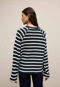 Sweter w paski w kolorze granatowym i białym, dzianinowa struktura, rękawy raglanowe oraz okrągły dekolt. Z tyłu znajdują się długie rękawy i luźny fason.
