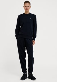 Zestaw dresowy w kolorze navy, wykonany z miękkiego materiału. Sweter ma ściśnięte mankiety i dół, z małym logo na klatce piersiowej. Spodnie są zwężane.