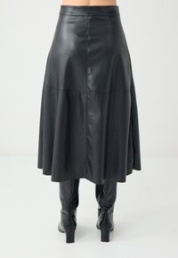 Zwarte leren midi-rok met een geflurde silhouet. Heeft stikseldetails en een soepele textuur. Gepaard met hoge zwarte laarzen.