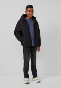 Schwarze Pufferjacke mit Kapuze, mit gestepptem Design und Frontreißverschluss, kombiniert mit einem blauen T-Shirt und dunklen Jeans. Legere Schuhe inklusive.