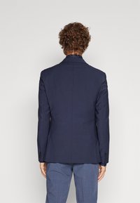 Navy blue tailored blazer with notch lapels and two back vents, made of textured fabric, worn over a light blue patterned shirt.