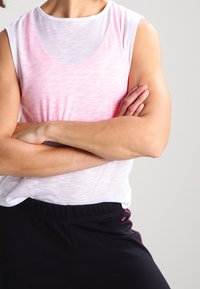 Lightweight, sleeveless athletic top in pale pink and white with a relaxed fit; paired with black pants featuring pink stitching accents.