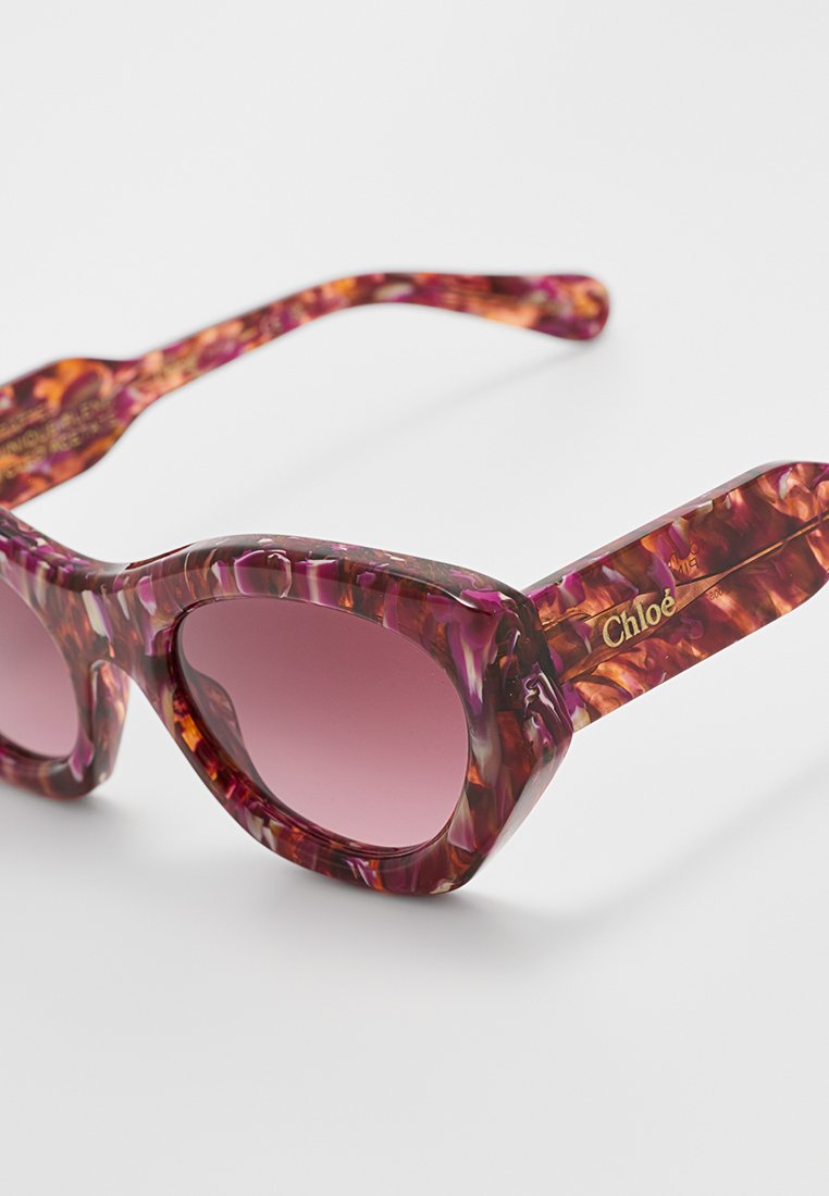 Fioletowo-różowe okrągłe okulary przeciwsłoneczne w kształcie kocich oczu, z gradientowymi soczewkami i złotym logo "Chloé" na zausznikach.