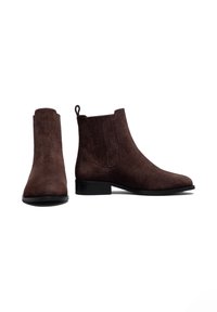 Bottes chelsea en daim marron à talon bas, avec des panneaux élastiques sur les côtés et une languette pour un enfilage facile. Texture lisse et design à bout arrondi.